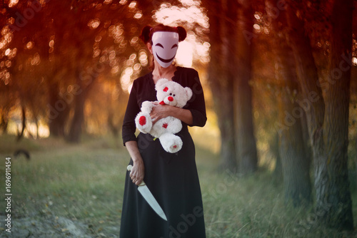 Creepy masked woman holding teddy bear with kitchen knife