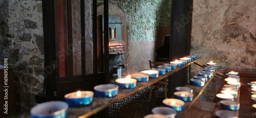 Lit tealight candles inside empty ancient stone chapel altar. Church shrine interior worship ritual, lighting candlelight. Burning prayer remembrance votive candle flame. Religious atmosphere ambiance