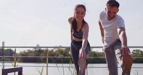 Sports exercises and training of fit couple of athletes before healthy jogging in summer park. Sporty happy woman and man runners in sportswear bend over together to stretch muscles and warm up