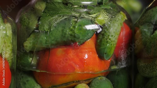 Home preservation. Assorted tomatoes with cucumbers in glass jars are poured with boiling water.