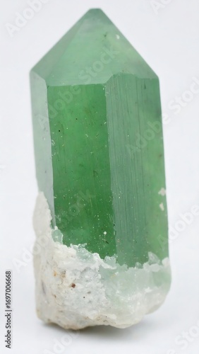A vibrant emerald green crystal, pointed at the top, rests on a bed of light gray mineral matter.