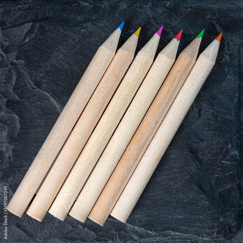 Group of colored pencils on textured dark surface, top view