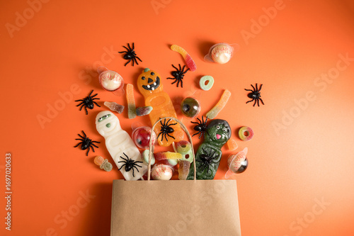 Halloween candies in paper bag over orange background, eye balls, warms, pumpkins. Flat lay.