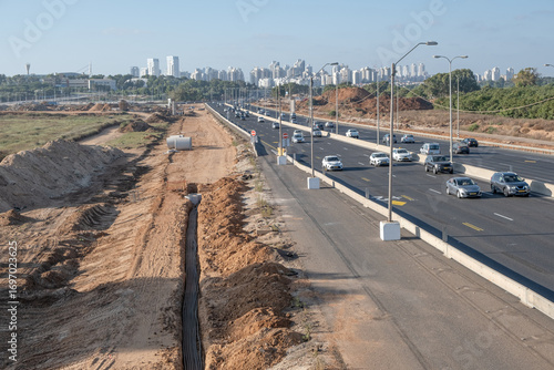 Multi-lane asphalt road in Netanya urban area with traffic, city infrastructure, and buried cable installation for digital systems