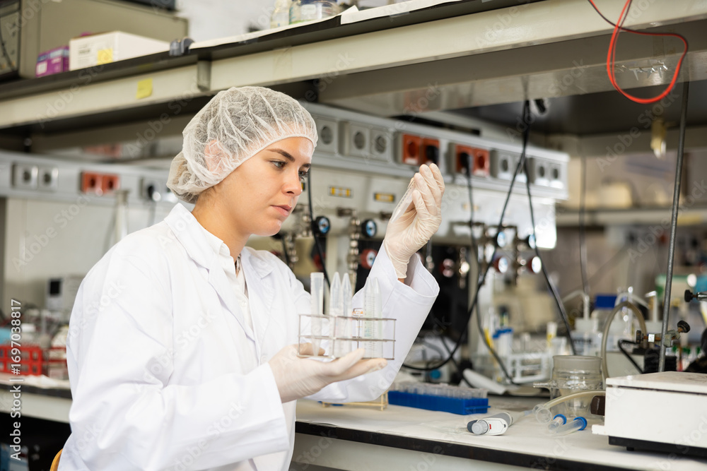 Fototapeta premium Portrait of young woman technical expert provide during work at science research laboratory, holding test tube and looking at it