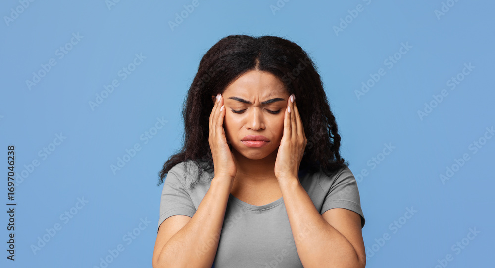© Prostock-studio - Headache and migraine concept. African american lady suffering from hypertension over blue studio background, free space. Overworked woman feeling stressed, going through emotional crisis