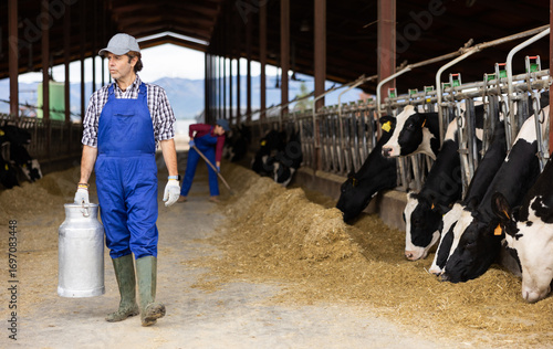 Dairy farmer man carrying aluminum can of milk in cowshed