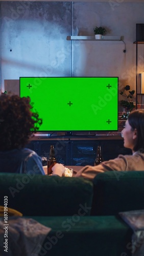 Two people watching a green screen TV in a living room