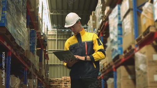 Professional male worker wearing  safety helmet working industrial warehouse storing and distributing logistics goods warehouse center using laptop record and monitor goods on the shelves.