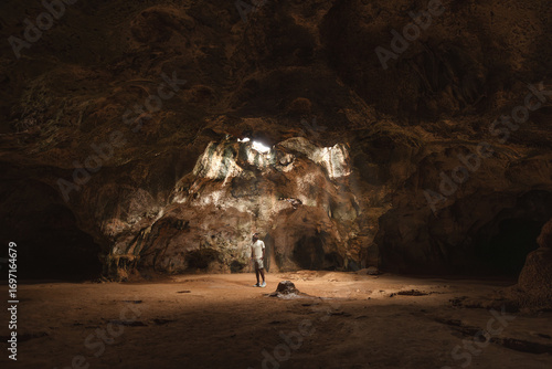 Hombre latino, viajero bajo los haces de luz  explorando la cueva Quadirikiri en el parque Nacional de Arikok, Aruba