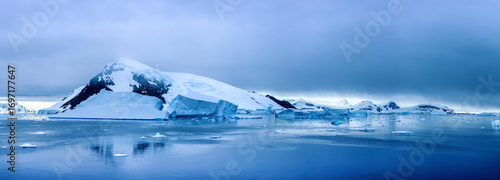 Panoramic view of the Antarctic landscape with snow-covered mountains, floating icebergs, and calm polar waters