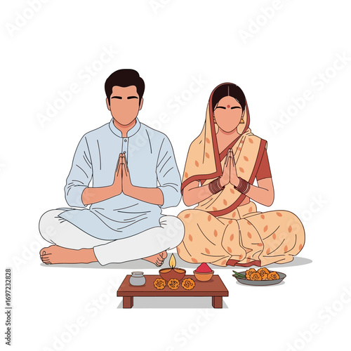 A couple in traditional Indian clothing sitting in prayer position with offerings on a small table.