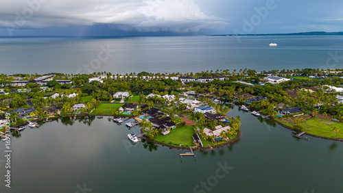 Dramatic aerial view of an exclusive waterfront community with luxury homes and private docks, under a dark, ominous sky as a storm approaches over the ocean
