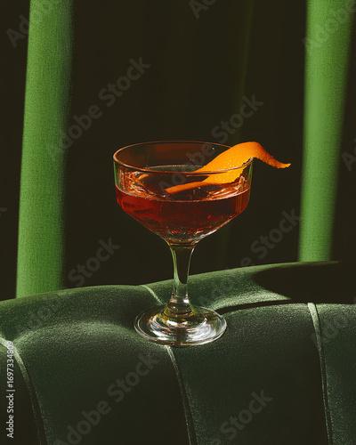Red cocktail in elegant coupe glass with orange peel garnish on green velvet