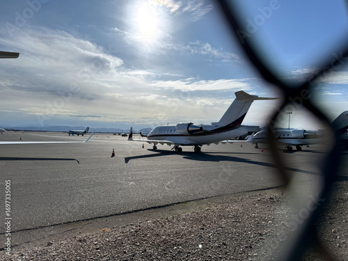 airplane at the airport through a chain link fence - general aviation airfield with jet planes on the tarmac