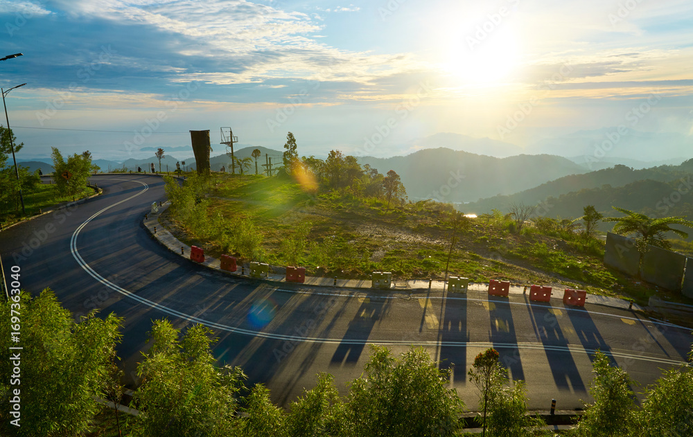 Naklejka premium Winding mountain road at sunrise illuminating lush green landscape