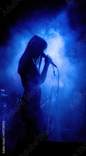 Silhouette of a female singer with a microphone in a smoky blue stage setting with musical equipment in the background