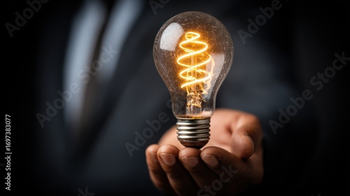 Wallpaper Mural Hand holds illuminated light bulb, showcasing a bright, spiral filament against a dark background Torontodigital.ca