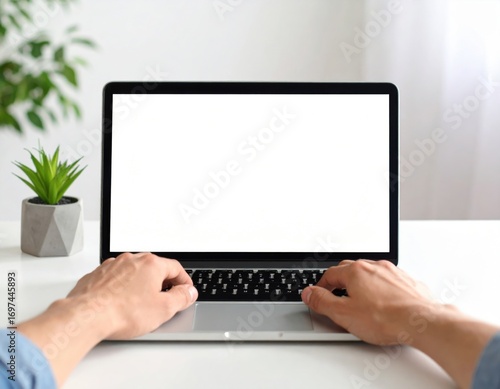 A first-person perspective of hands on a keyboard with a modern laptop featuring a blank white screen for mockups on a clean desk.