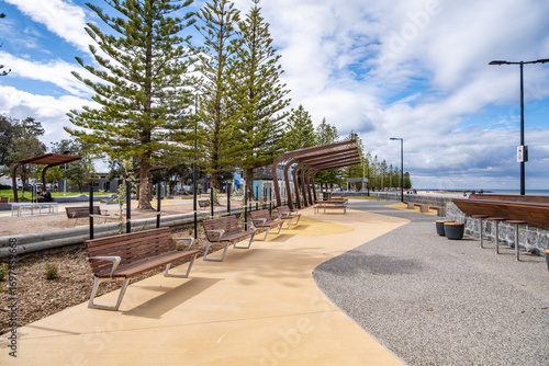 Modern public seating and shaded facilities along the Altona foreshore in Melbourne, Australia. Featuring wooden benches, architectural shade structures at the rest area, and pedestrian pathways. 