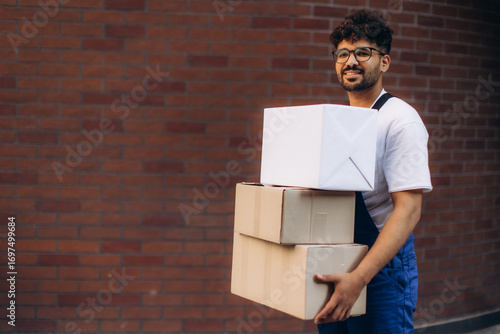 Delivery man carrying cardboard boxes in front of brick wall
