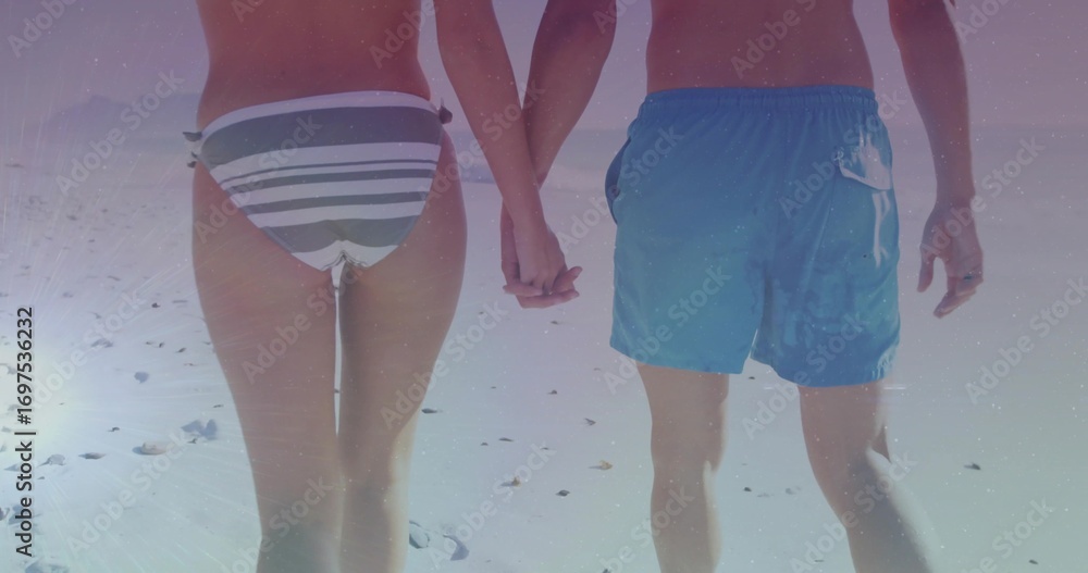 Fototapeta premium Walking couple holding hands along sandy beach, with striped bikini bottom, swim trunks and shells