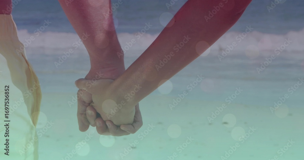 Fototapeta premium Holding hands of couple wearing light beach shorts, pink sleeveless top in shallow surf, soft flare