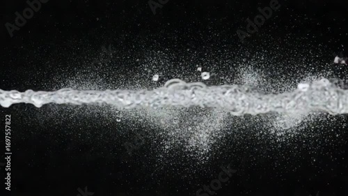 A powerful horizontal jet of clear water splashing and creating droplets against a stark black background.