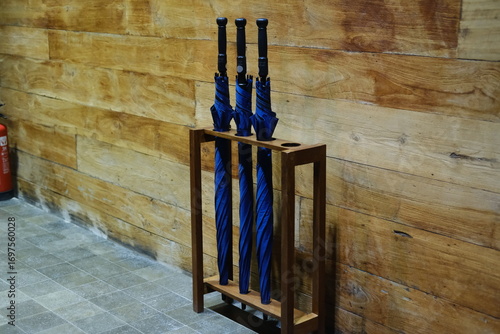 Three Blue Umbrellas in Wooden Stand Against Wooden Wall