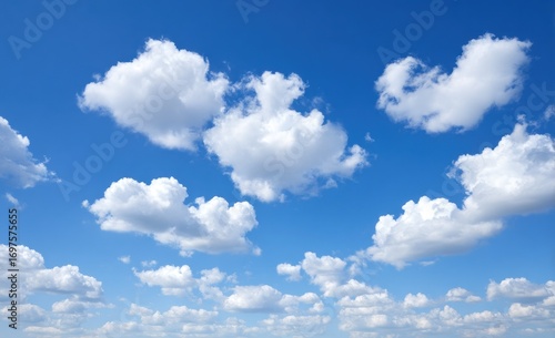 Puffy white cumulus clouds drift across a bright, vivid blue sky. Sunny day aerial perspective features airy, light textures