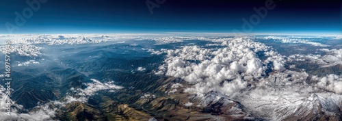 Aerial panorama of mountain range partially covered in clouds under a clear blue sky, capturing a scenic and ethereal landscape