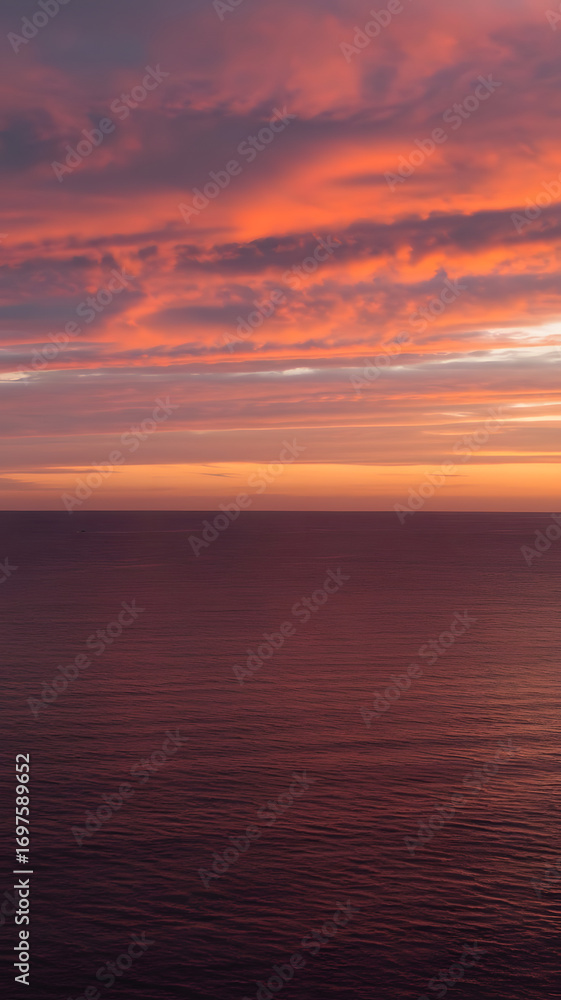 Fototapeta premium A tranquil seascape at twilight with a dramatic, fiery sky of orange and pink clouds reflecting on the calm, endless ocean