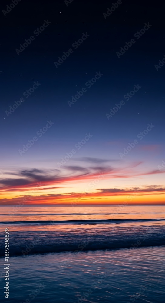 Obraz premium Tranquil ocean waves gently lap shore under a breathtaking twilight sky painted with vibrant sunset hues and distant stars emerging