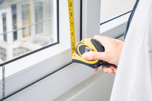 A man's hand is measuring a window with a tape measure.