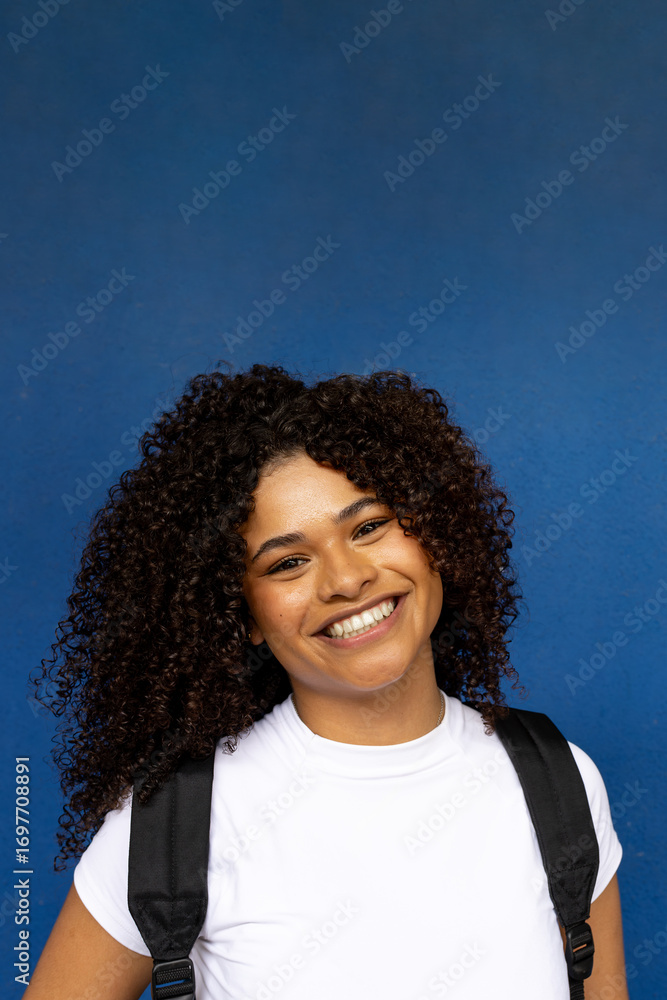 Fototapeta premium Young student smiling with backpack on blue background