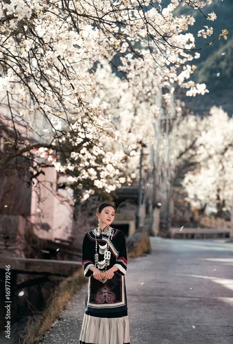 Fotografie Woman in traditional dress standing gracefully beneath blooming trees