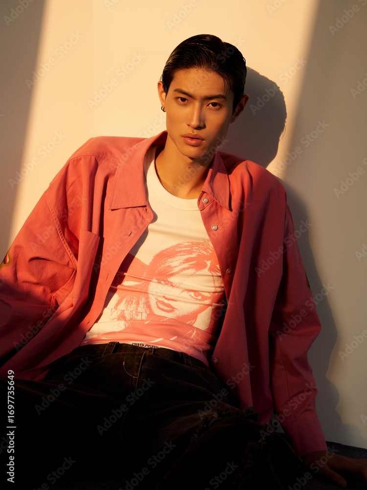 Fototapeta premium Stylish man in pink shirt and graphic tee sitting casually against a wall.