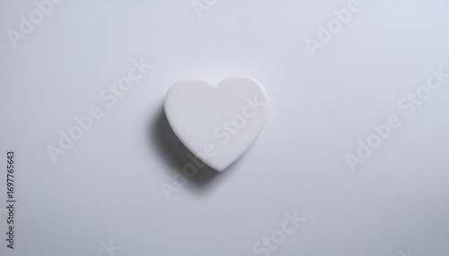 White heart shaped tablet rests on smooth white paper background viewed from above, creating a serene and minimalistic visual