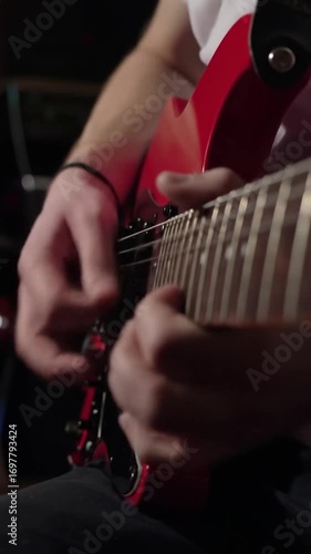 Close-up of hands playing red electric guitar, focus on fretboard and strumming