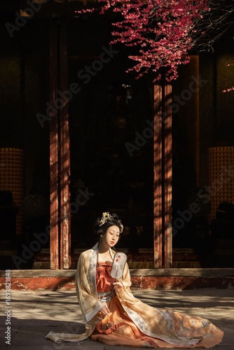 Tableau sur toile Elegant woman in traditional hanfu dress sitting outdoors under cherry blossoms
