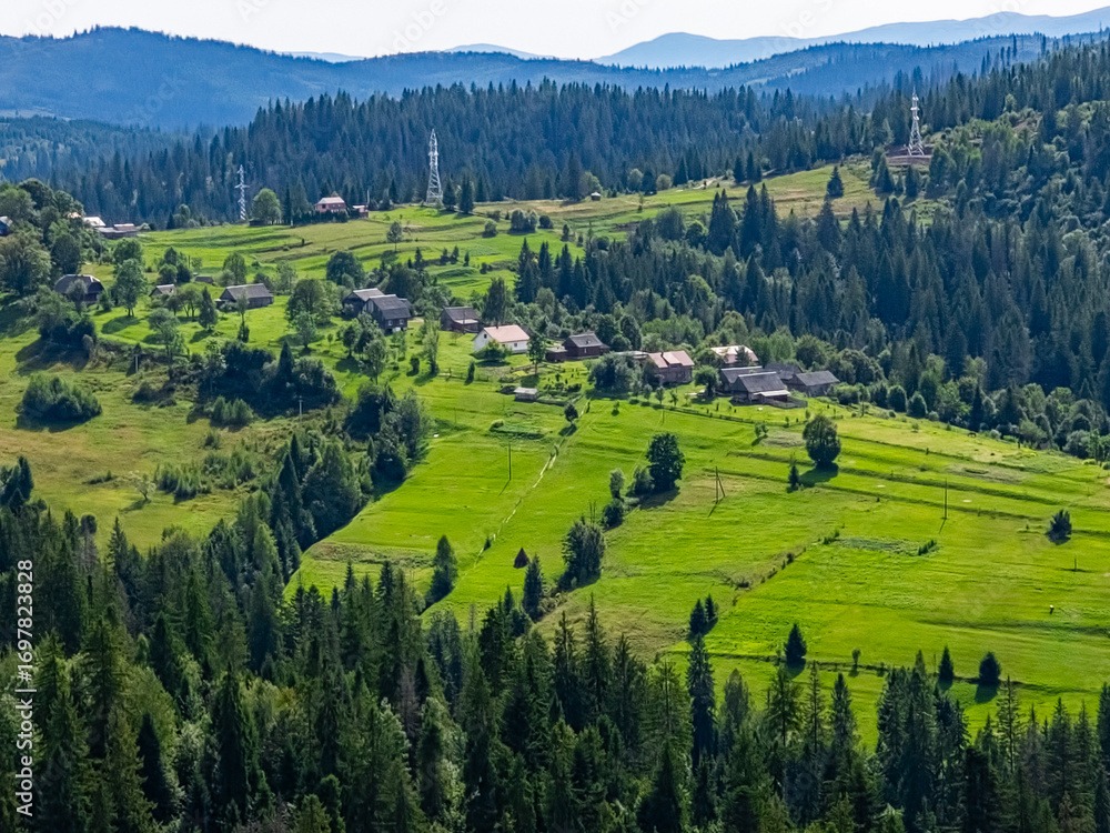 Obraz premium A stunning view of a mountain village nestled among rolling hills and wildflowers, perfect for travel promotions, eco-tourism, and nature retreats