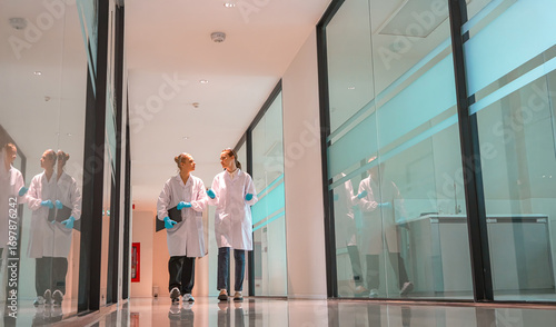 Two scientists in lab coats walk side by side through a sleek laboratory corridor