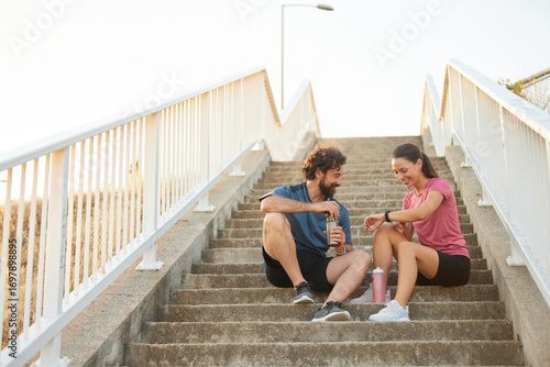 Fotografie Two individuals are sitting on outdoor steps, enjoying a moment of relaxation after exercising