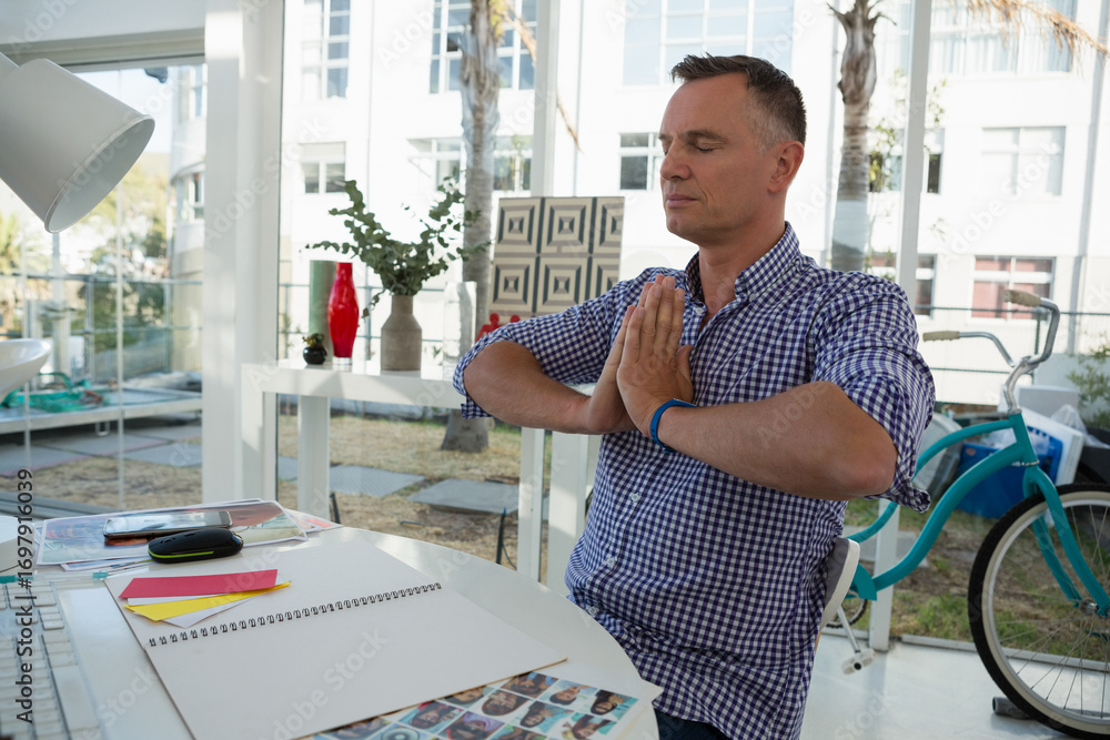 Naklejka premium Meditating man holding prayer pose at home office desk, with sketchbook and bicycle, copy space
