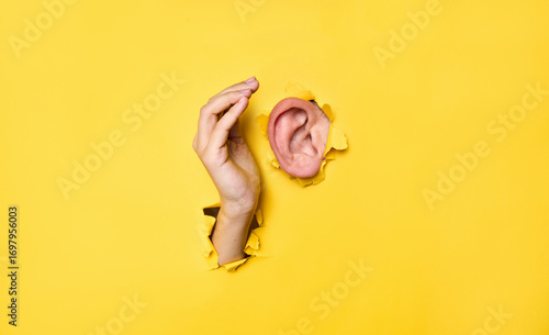 Close-up of  human ear and hand through torn yellow paper