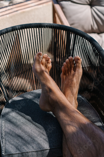 Tableau sur toile Relaxed bare feet of a man resting on a modern outdoor chair on a sunny day