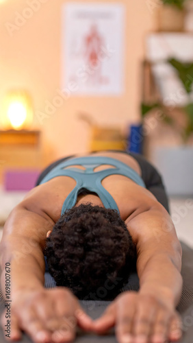Black woman stretching on yoga mat in child pose with relaxed expression and warm studio lighting
