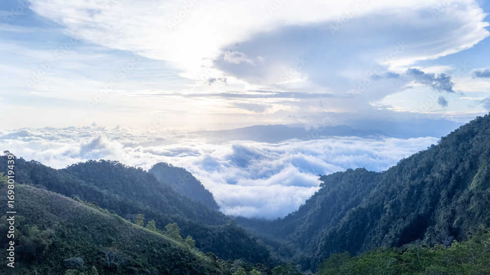 Fototapeta premium Dramatic view of a valley flanked by two hills, with thick clouds and hidden sunlight, creating a moody, atmospheric landscape perfect for nature and travel projects.