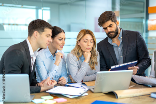 Dedicated business people in a meeting discussing strategy while reviewing data from laptop and reports