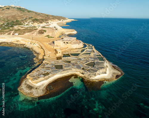 Aerial view of the ancient salt pans glisten under the Gozitan sun, contrasting sharply with the deep blue Mediterranean sea, Gozo, Gozo, Malta.